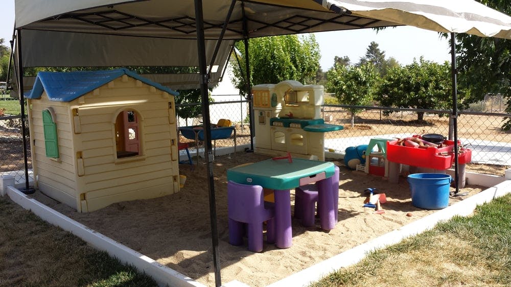 Play area with a playhouse, table, and sand under a canopy