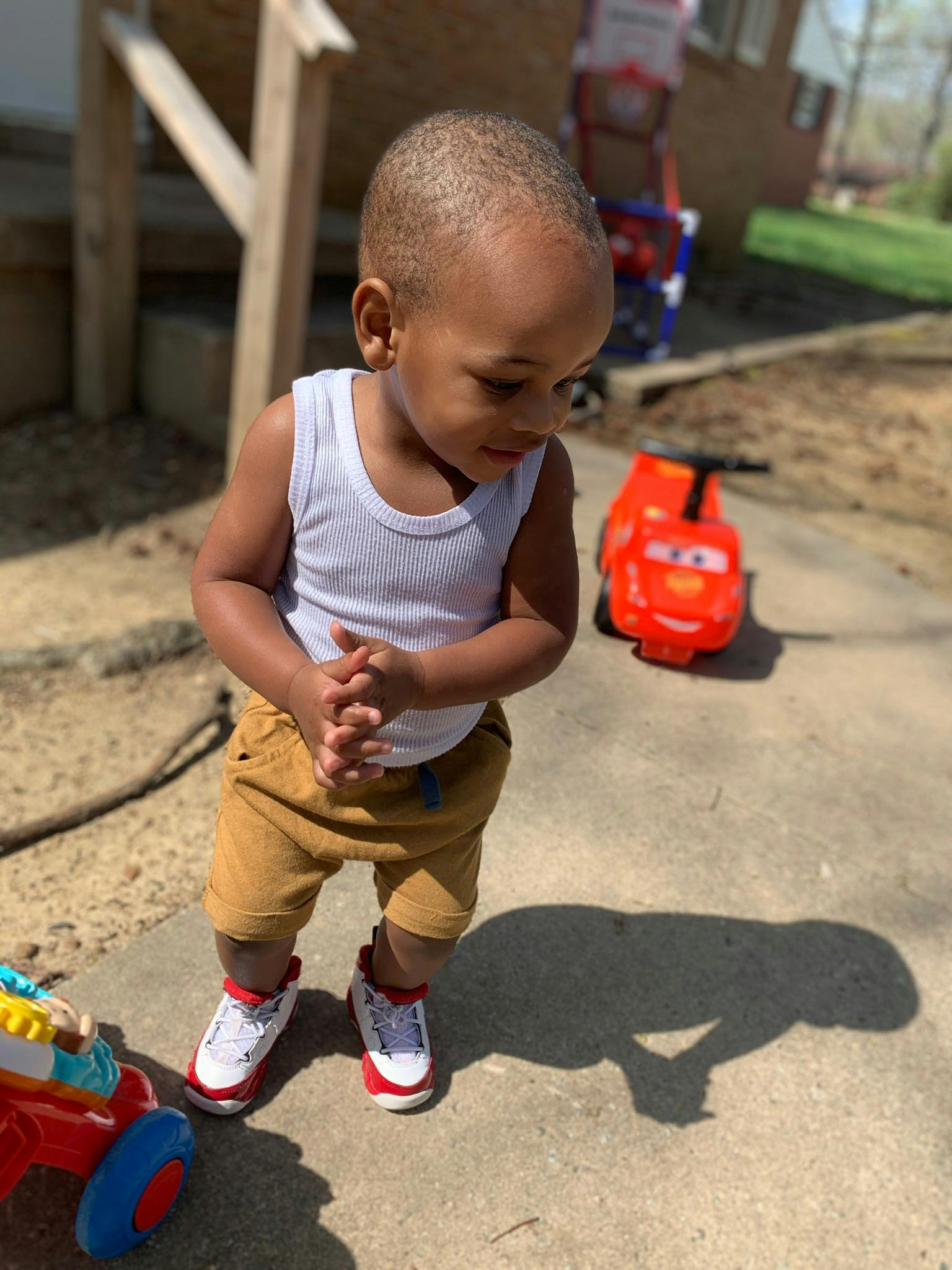 Child standing outdoors looking down with hands clasped