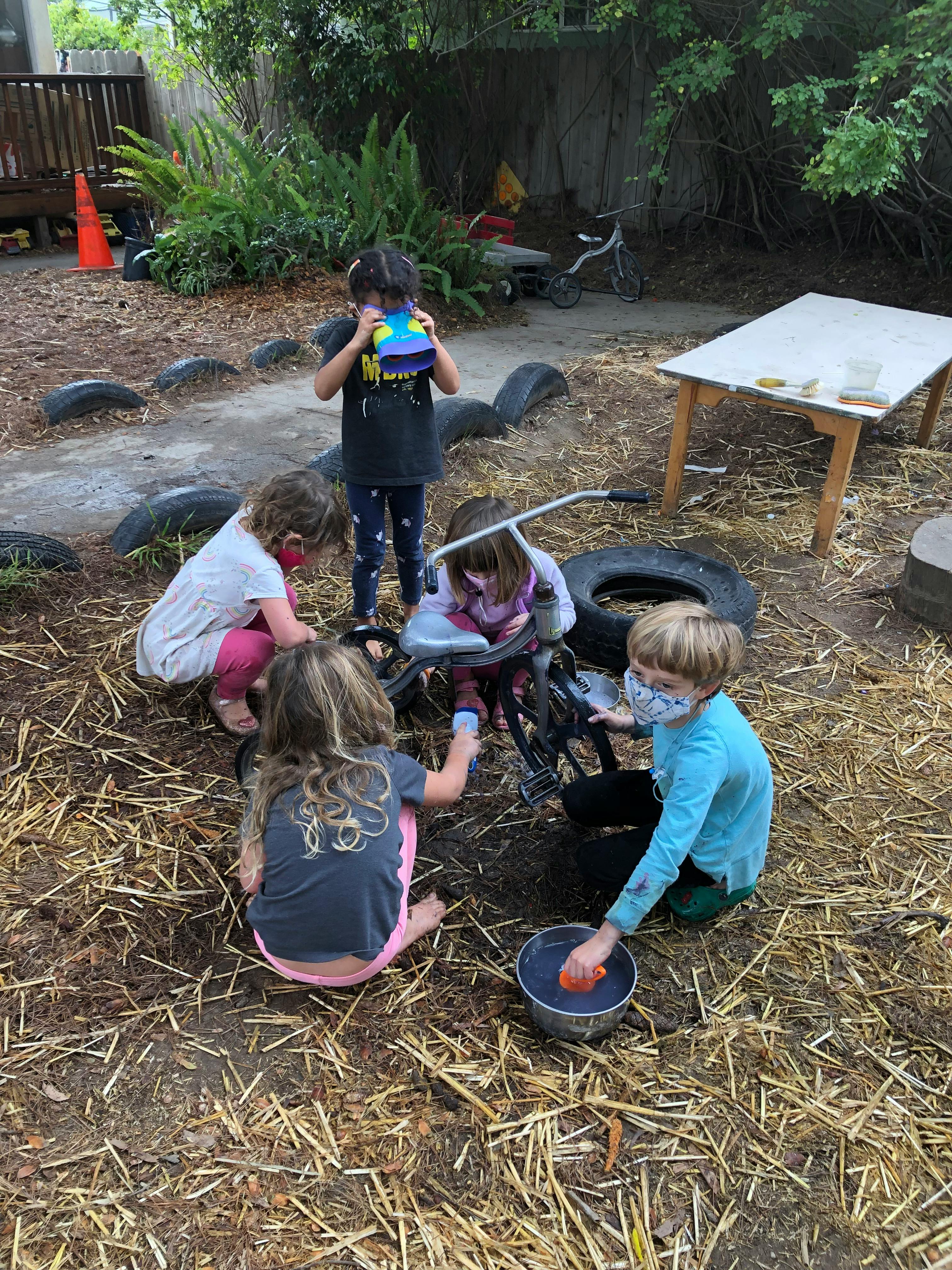Children playing outdoors with a tricycle and a bucket