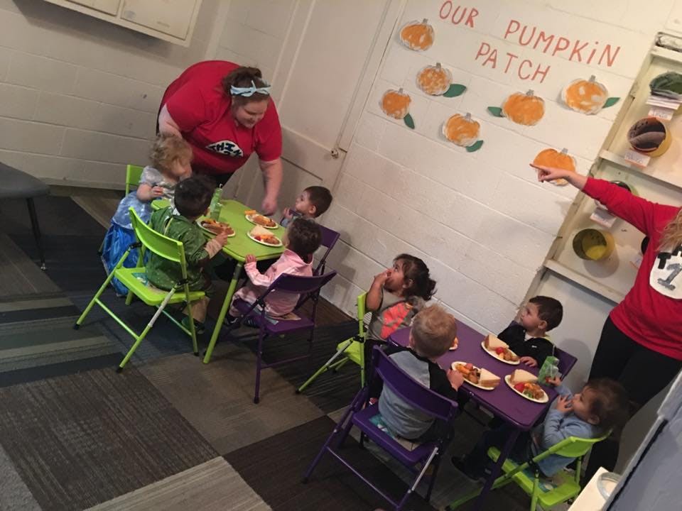 Adults and children eating at small tables in a room with pumpkin decorations
