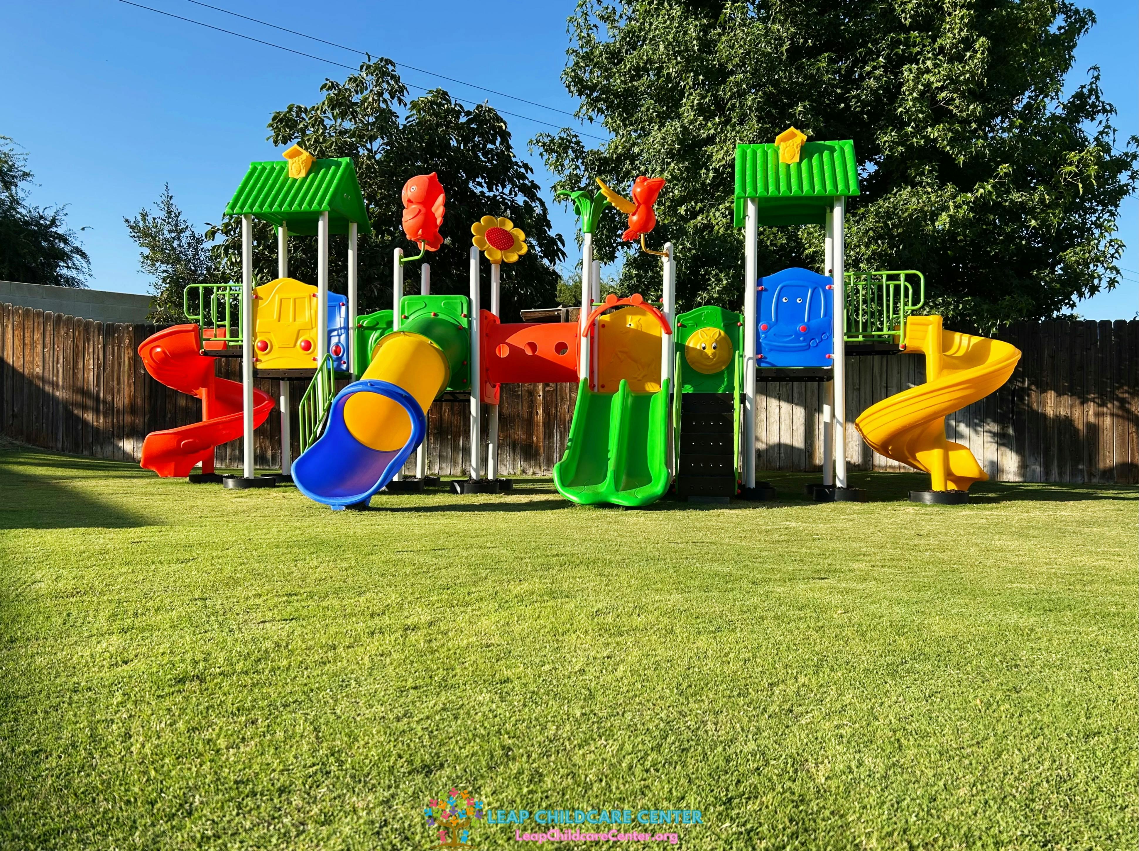 Colorful outdoor playground with slides, tunnels, and steps on a green lawn