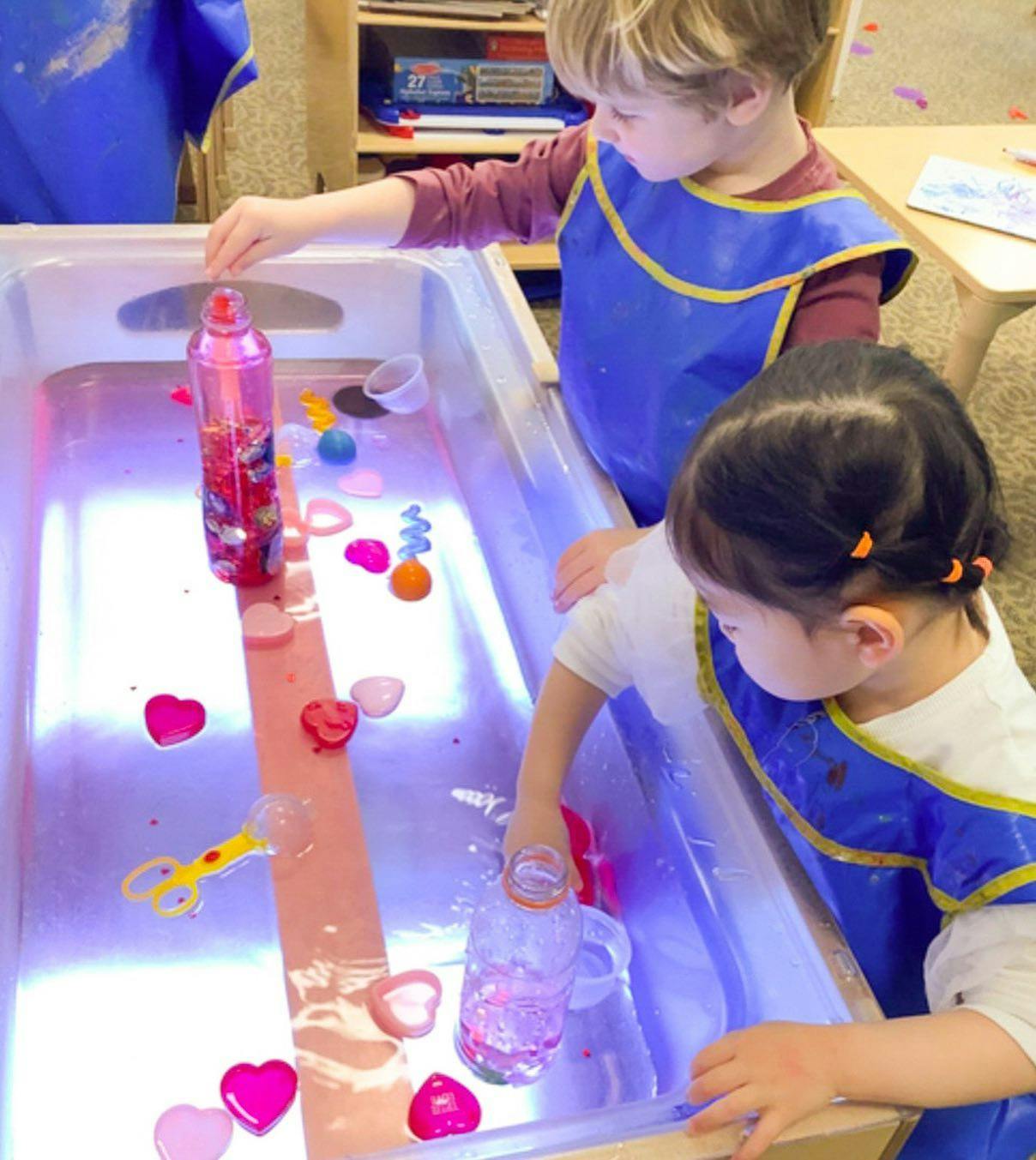 Two children playing with toys in a water table