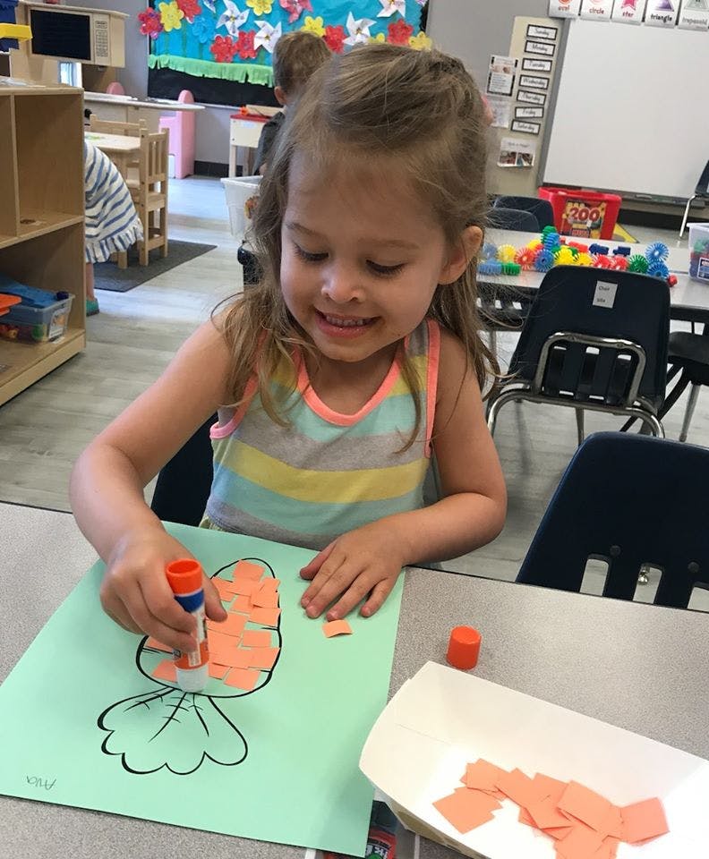 Child gluing orange paper pieces onto a drawing of a carrot