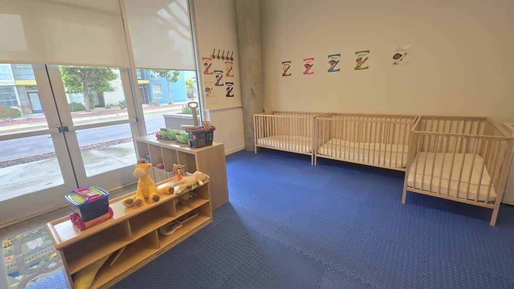 Nursery room with multiple cribs and shelves with toys