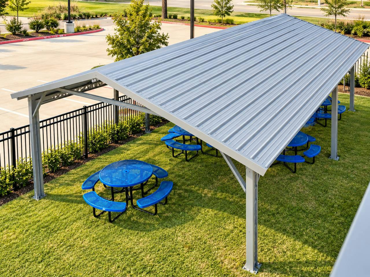 Covered metal pavilion with blue picnic tables on a grassy lawn