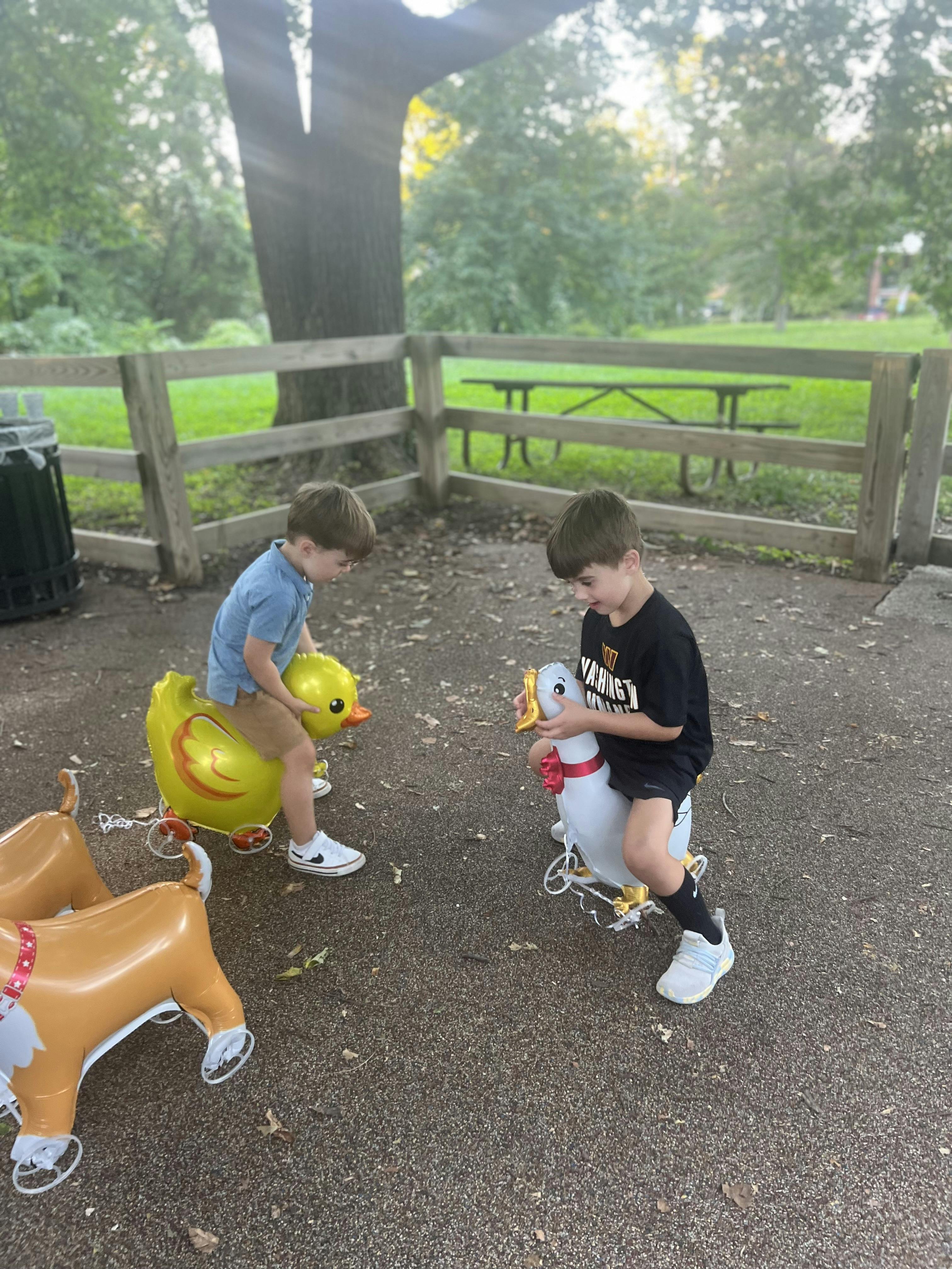 Two children riding inflatable animal toys outdoors