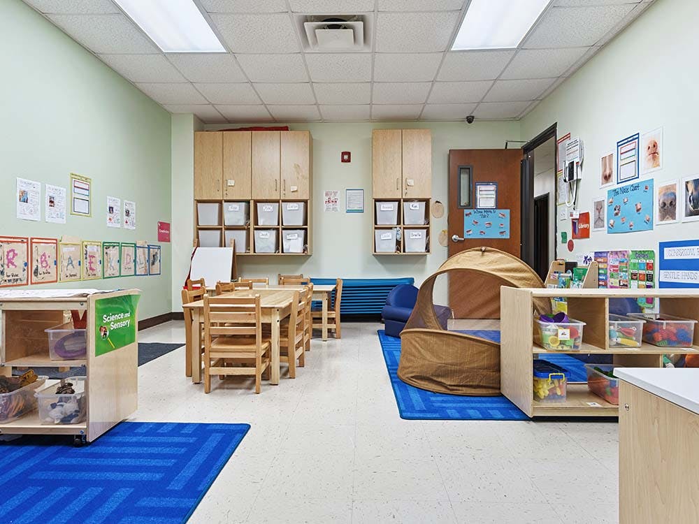 An empty classroom with small tables and chairs, shelves, and a tent