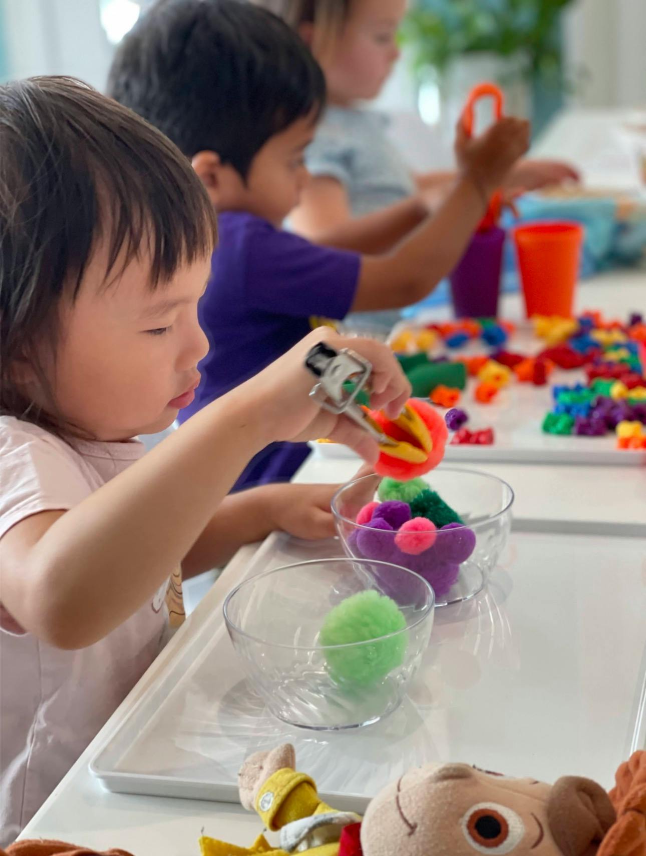 Children using tweezers to sort colorful pom-poms into bowls