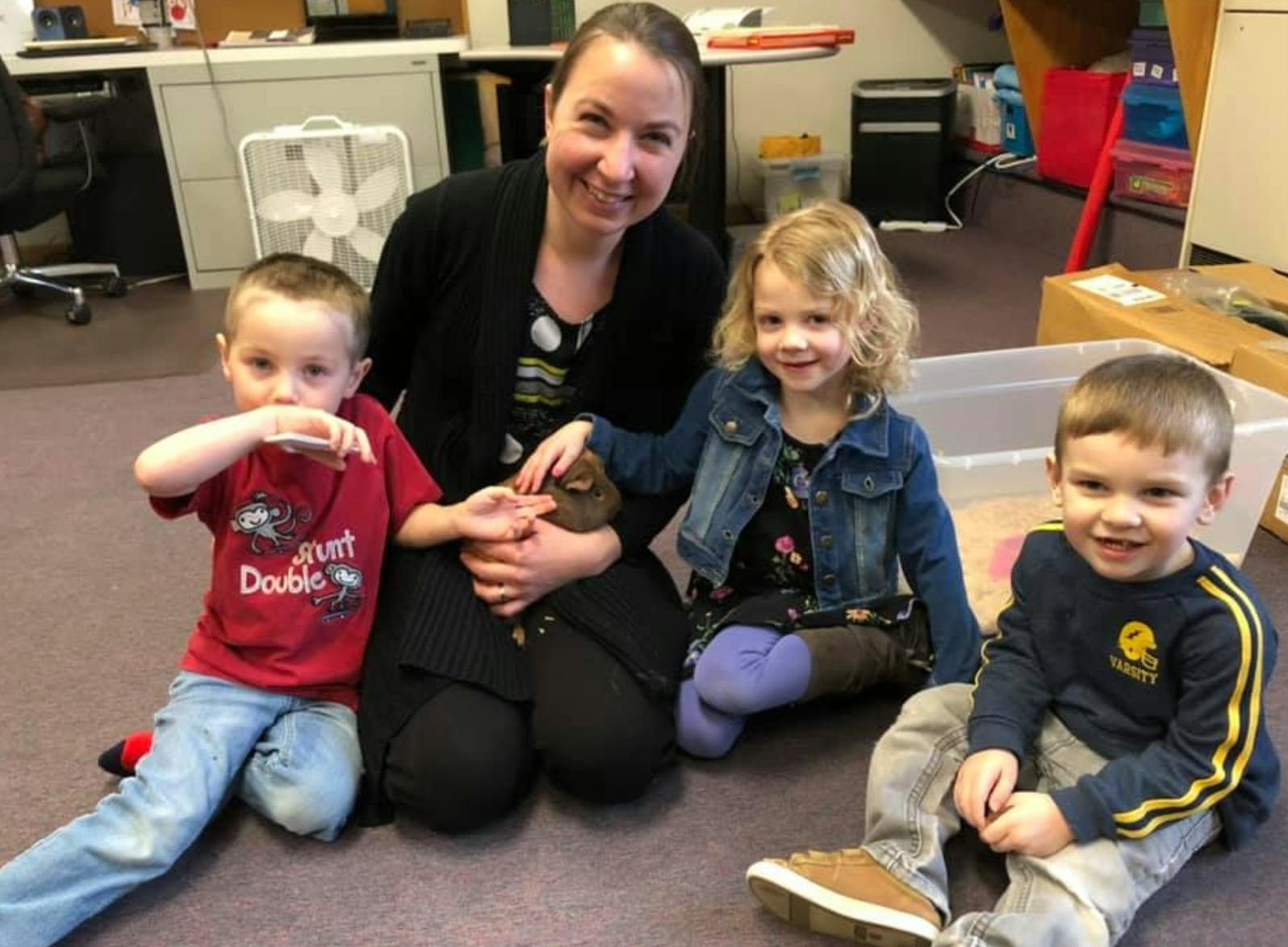 Person kneeling with three children sitting on the floor