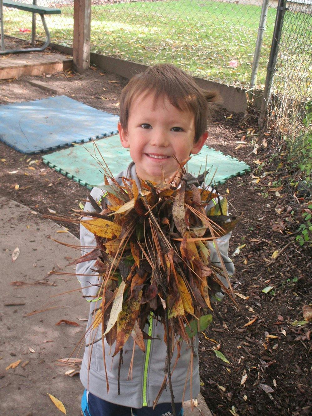 Child holding a large bundle of dried leaves and twigs