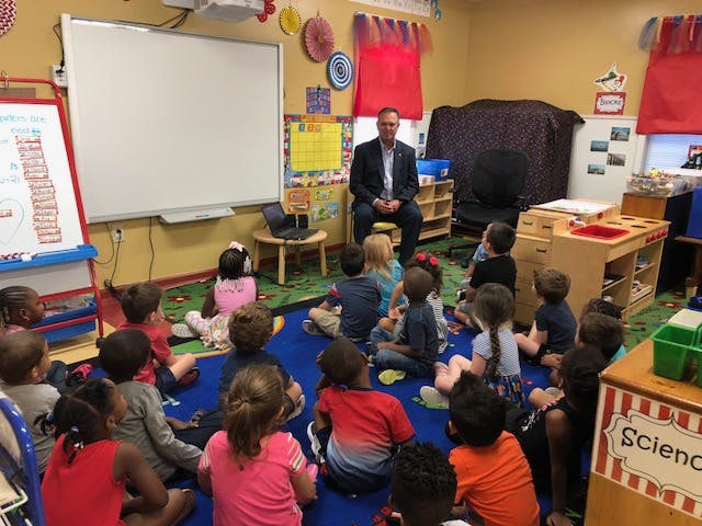 Adult sitting on a chair with children sitting on the floor in a classroom
