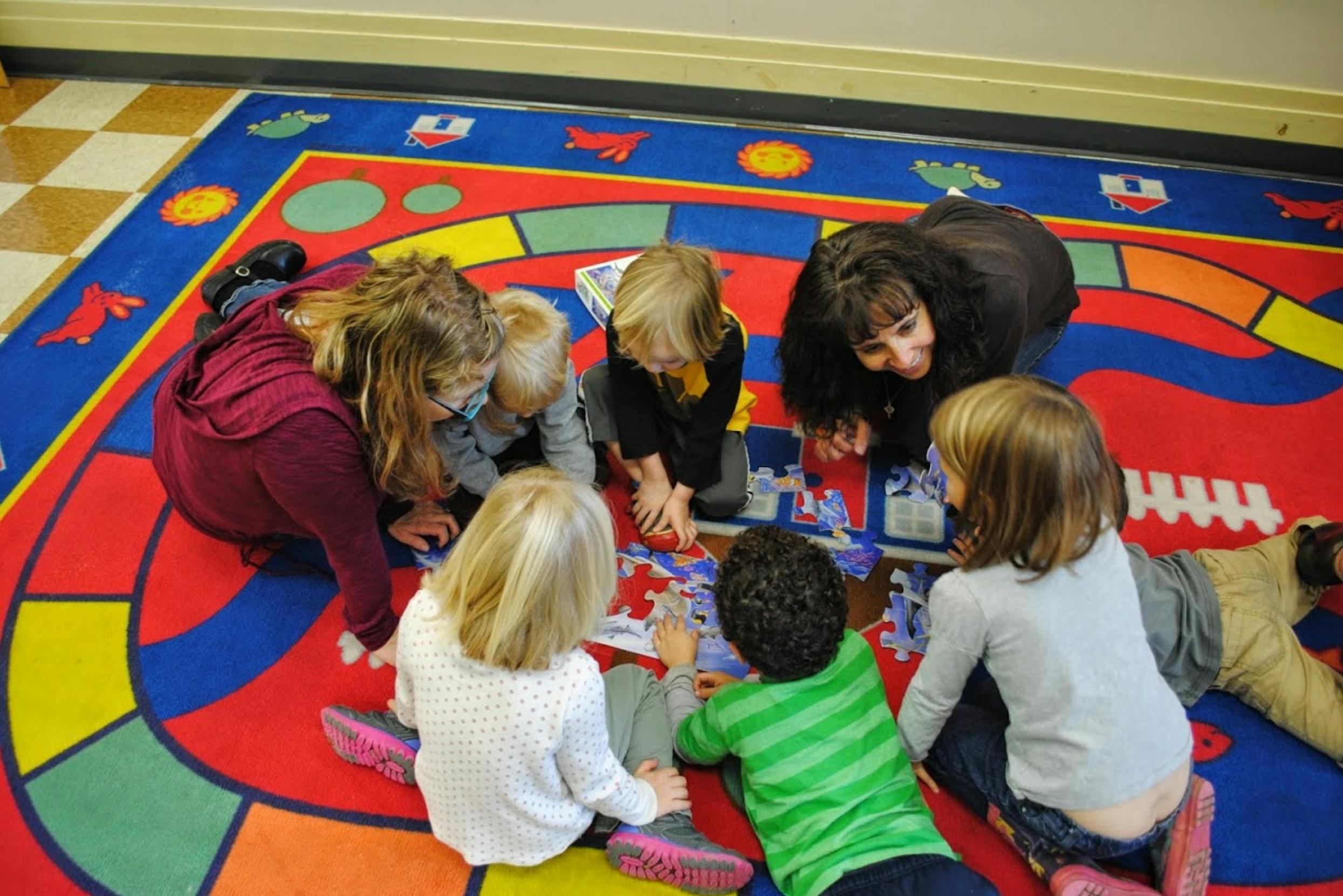 Group of children and adults playing a board game on a colorful rug