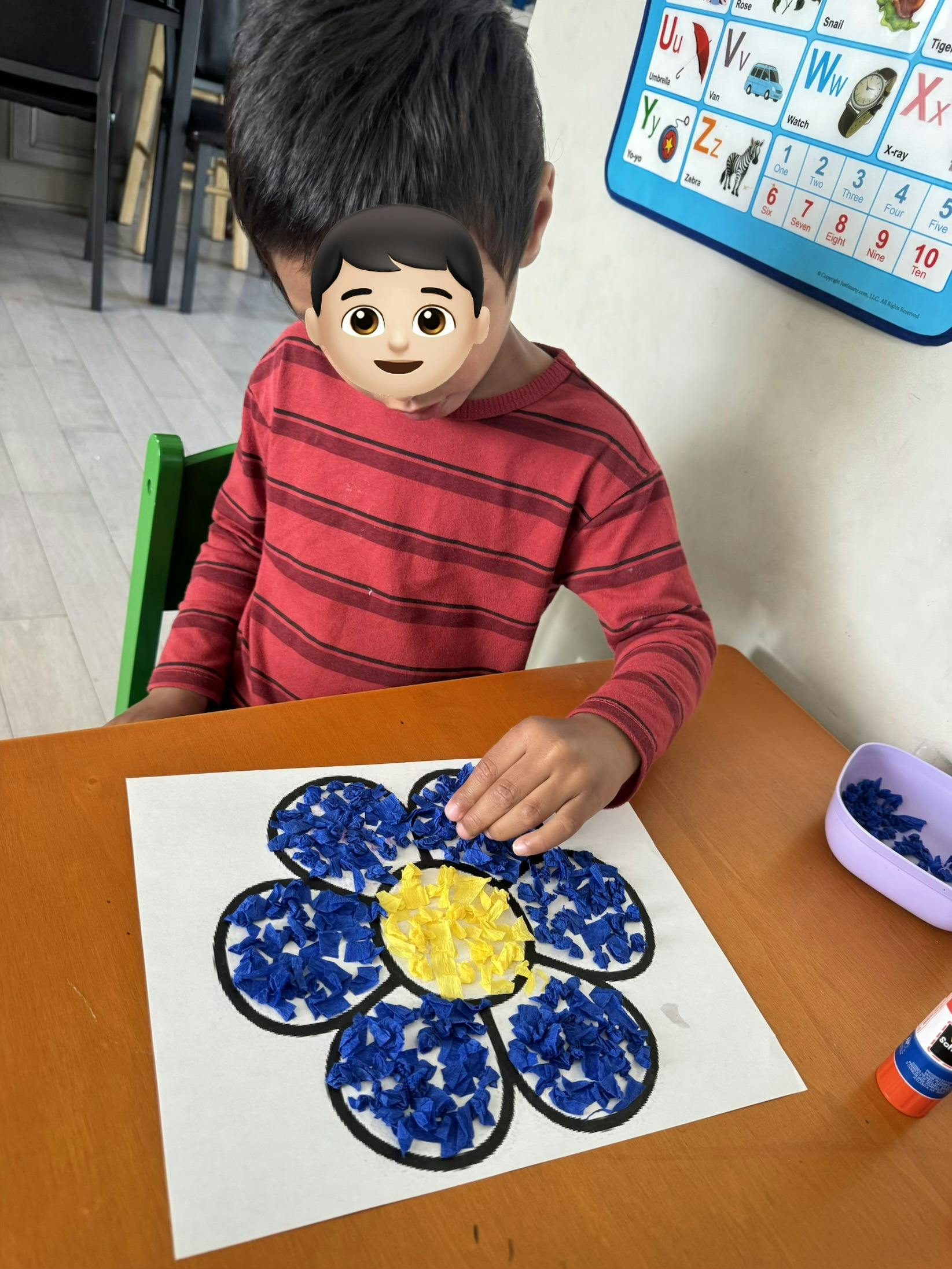 Child crafting a flower picture with blue and yellow tissue paper