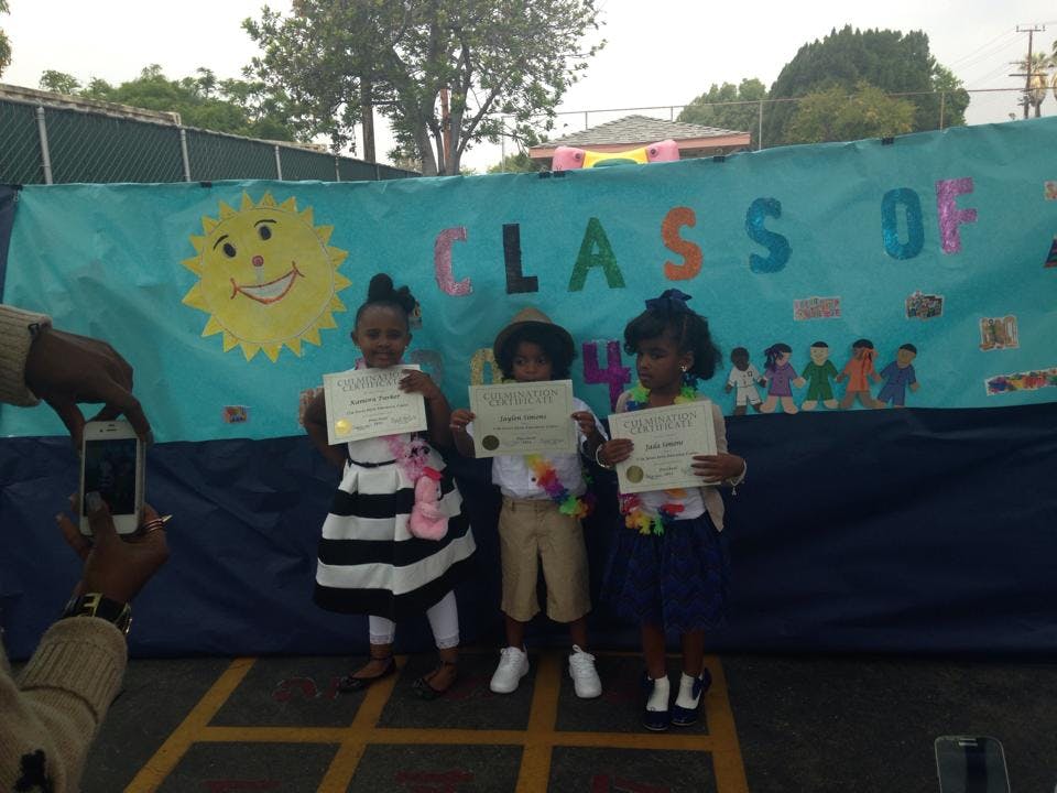 Three children holding certificates in front of a banner that says "CLASS OF"