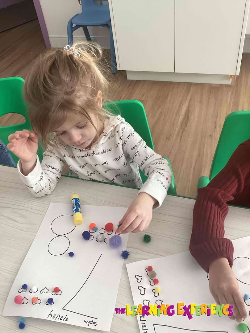 Child placing pom-poms on a paper with drawn shapes