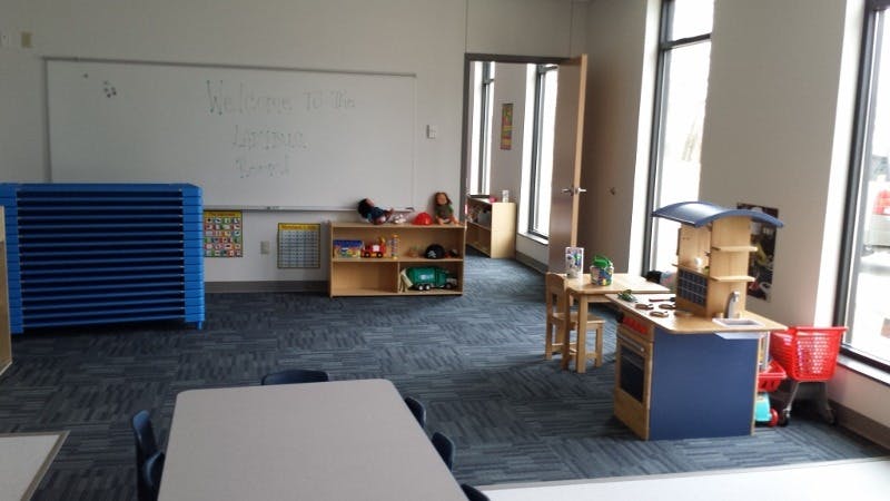 Classroom with whiteboard, blue mats, wooden shelves, and play kitchen