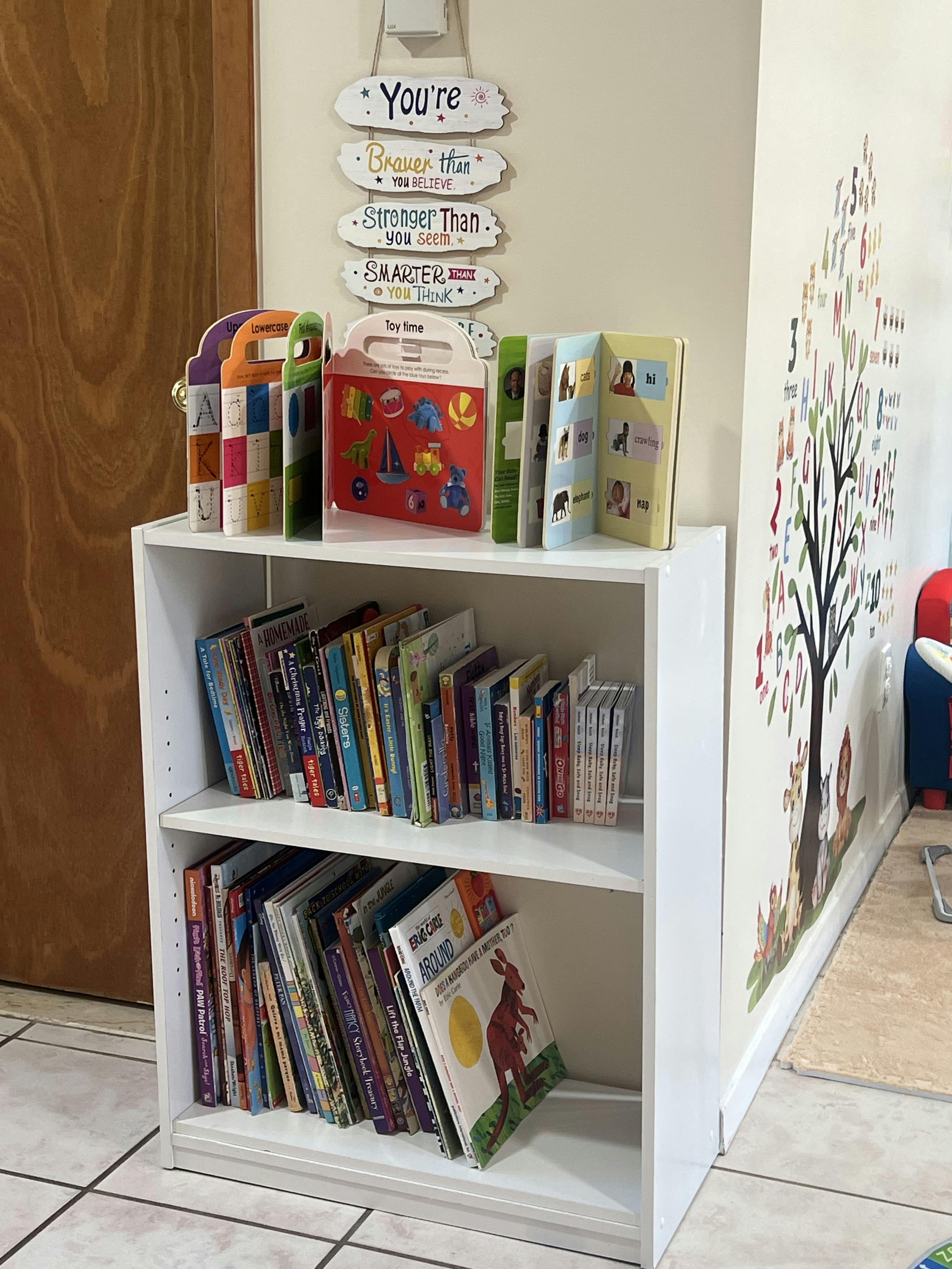 White bookshelf filled with children's books, with a wall decal of a tree
