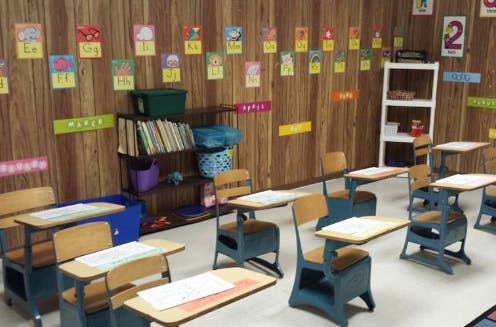 Empty classroom with small desks and chairs, shelves with books, and decorations on the wall