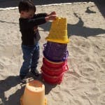 Child stacking colorful buckets in sand