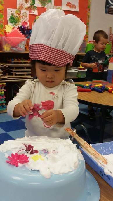Child in chef hat decorating a blue bowl with white foam and flower cutouts
