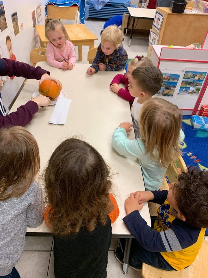 Adult showing a small pumpkin to children at a table in a classroom