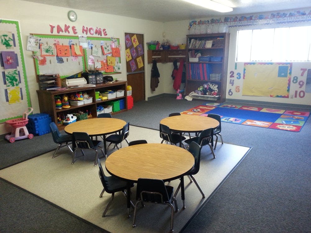 Classroom with small round tables and chairs, and a bulletin board with "TAKE HOME"