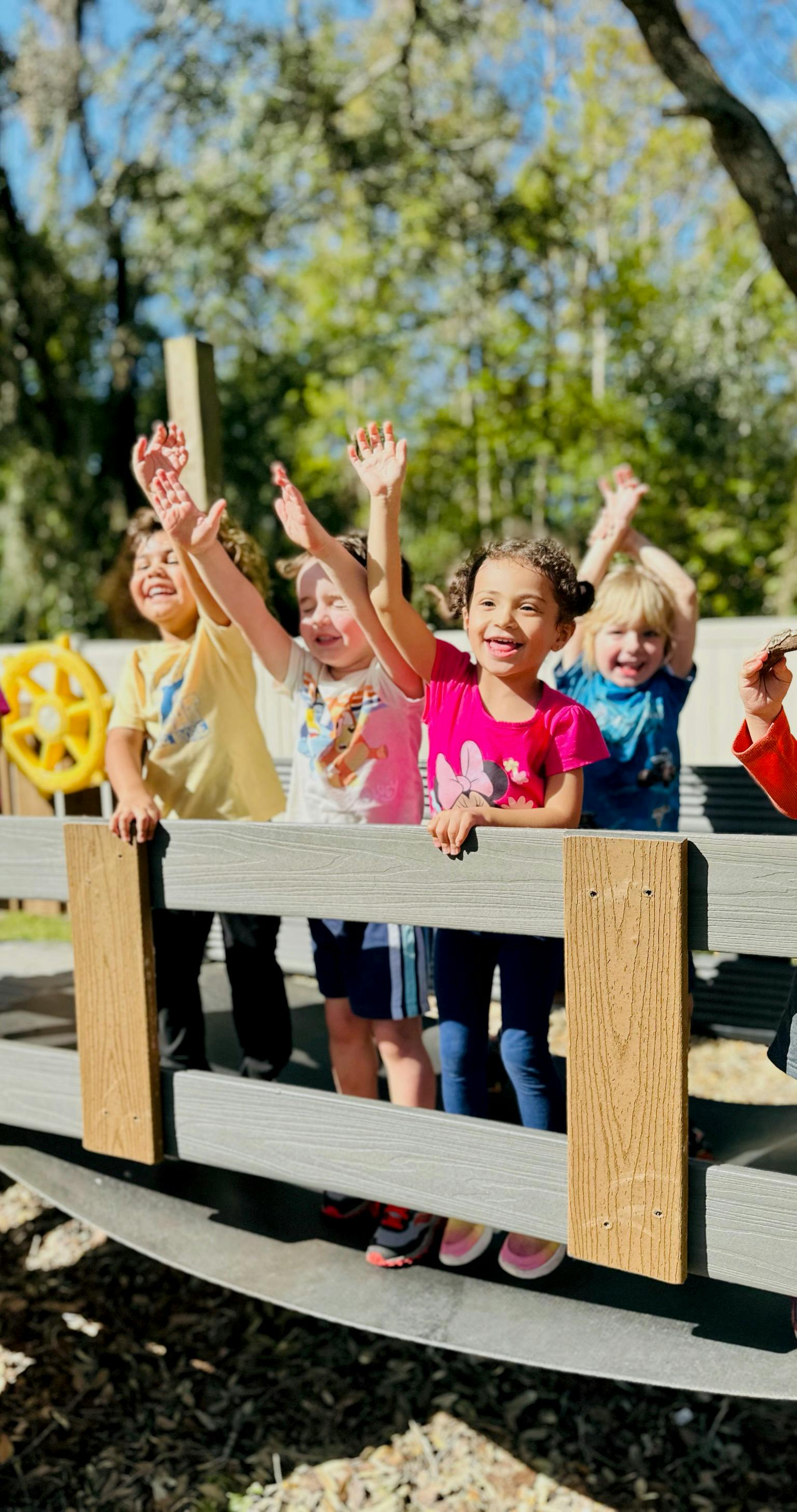 Children on a playground structure with hands raised