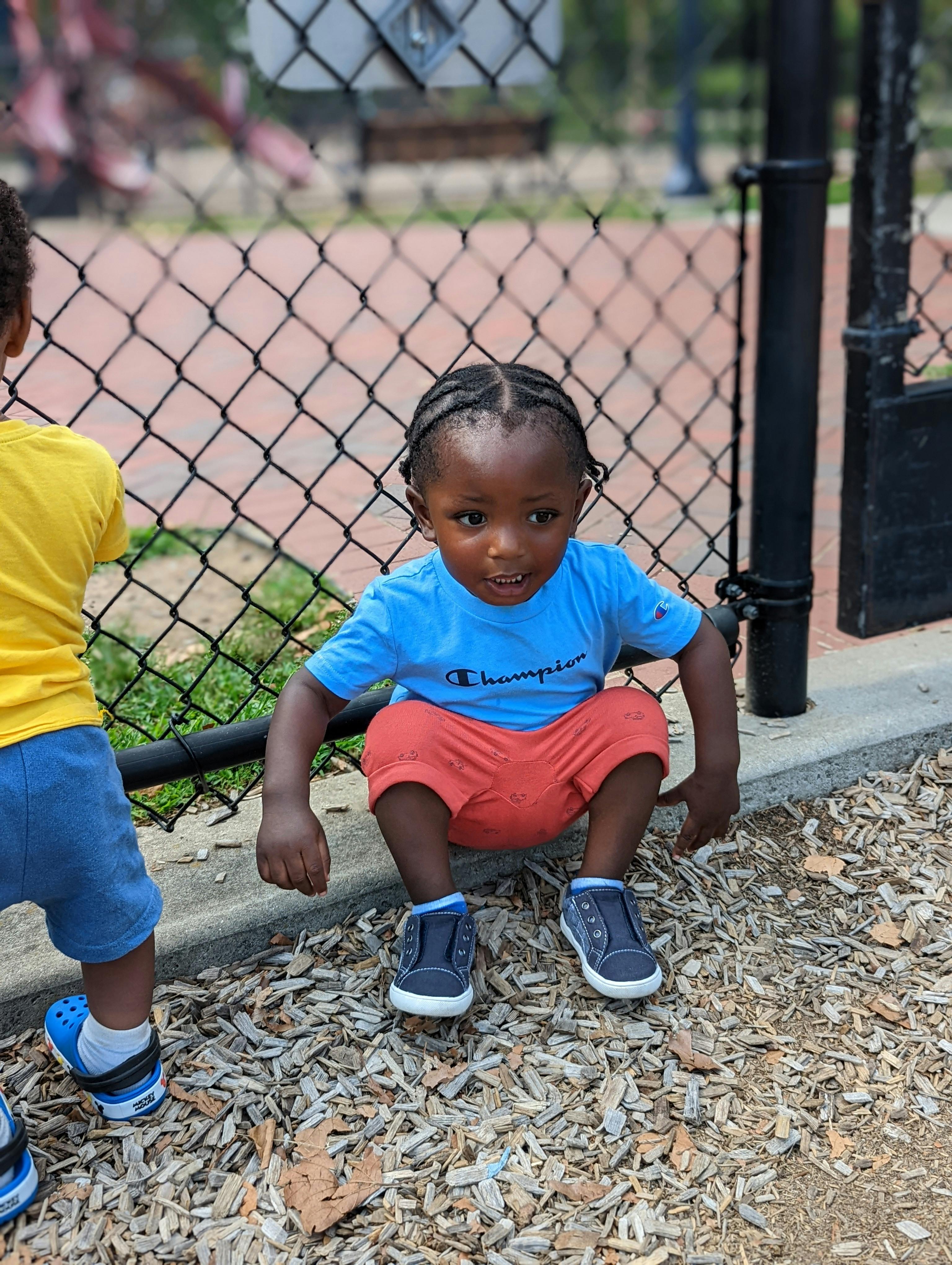 Child crouching on wood chips next to a fence