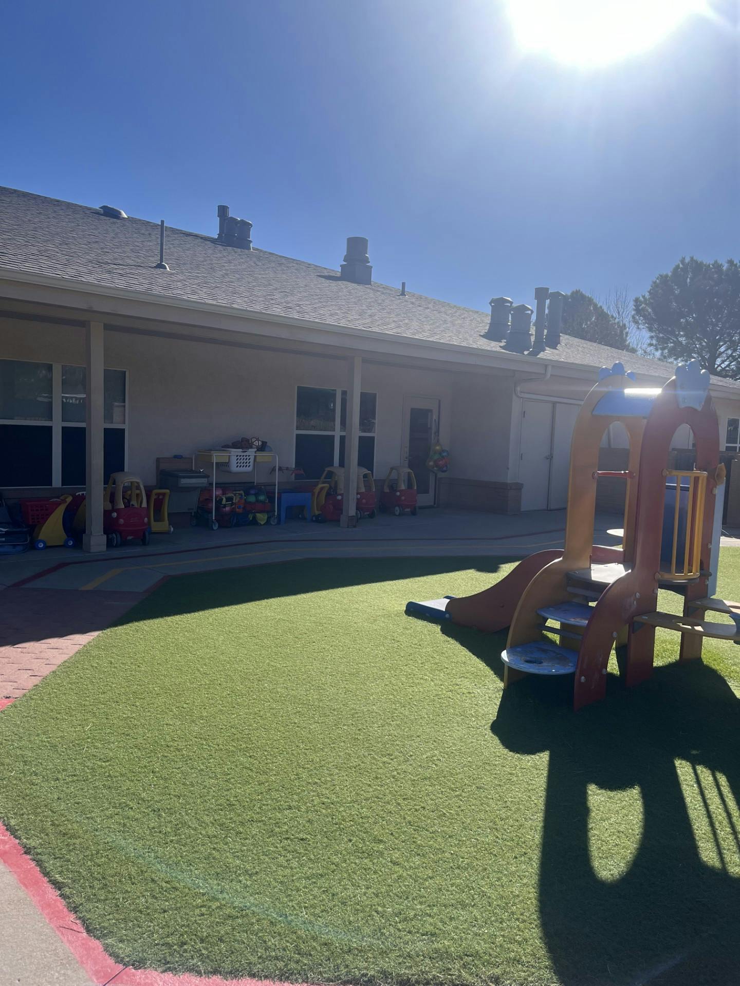 Playground with a slide and toy cars on artificial turf next to a building