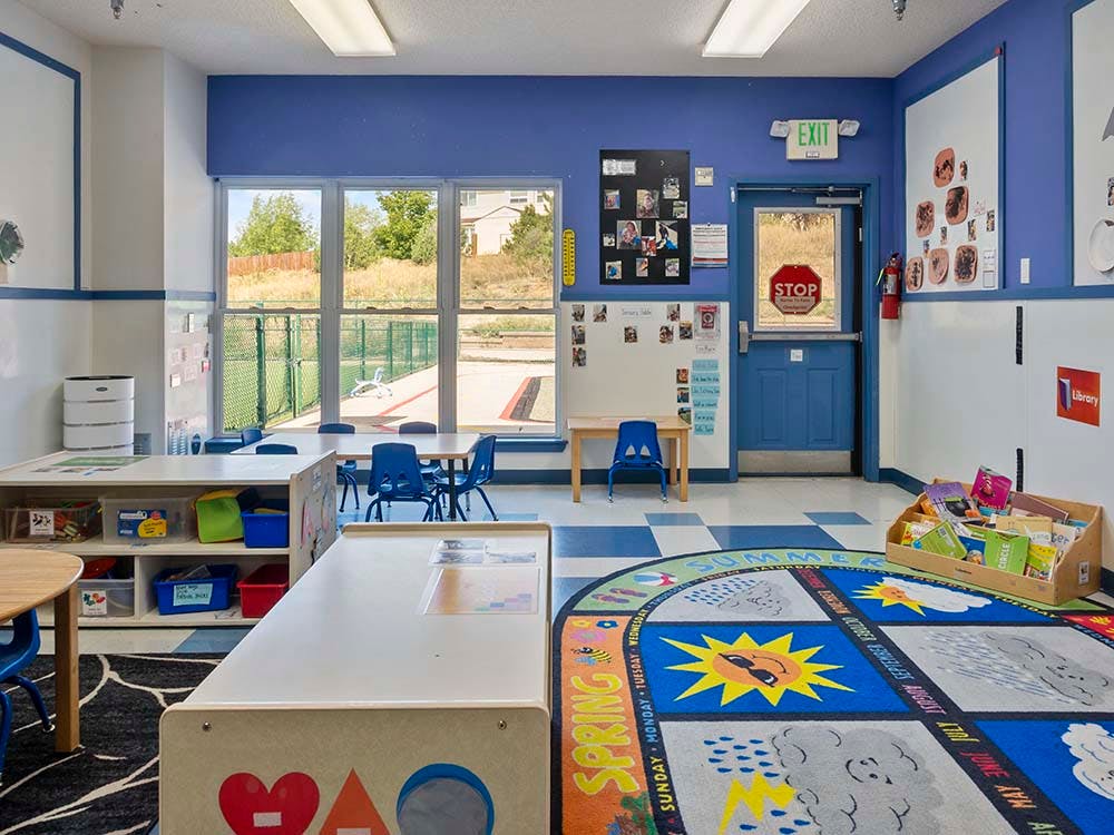 Classroom with tables and chairs, a large window, and an exit door
