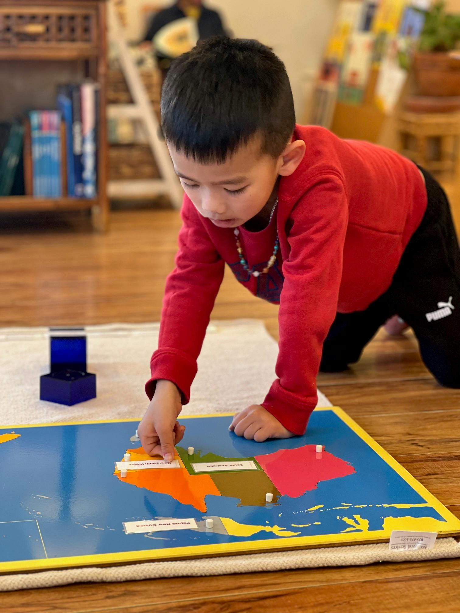 Child kneeling and placing a piece onto a Montessori world map puzzle