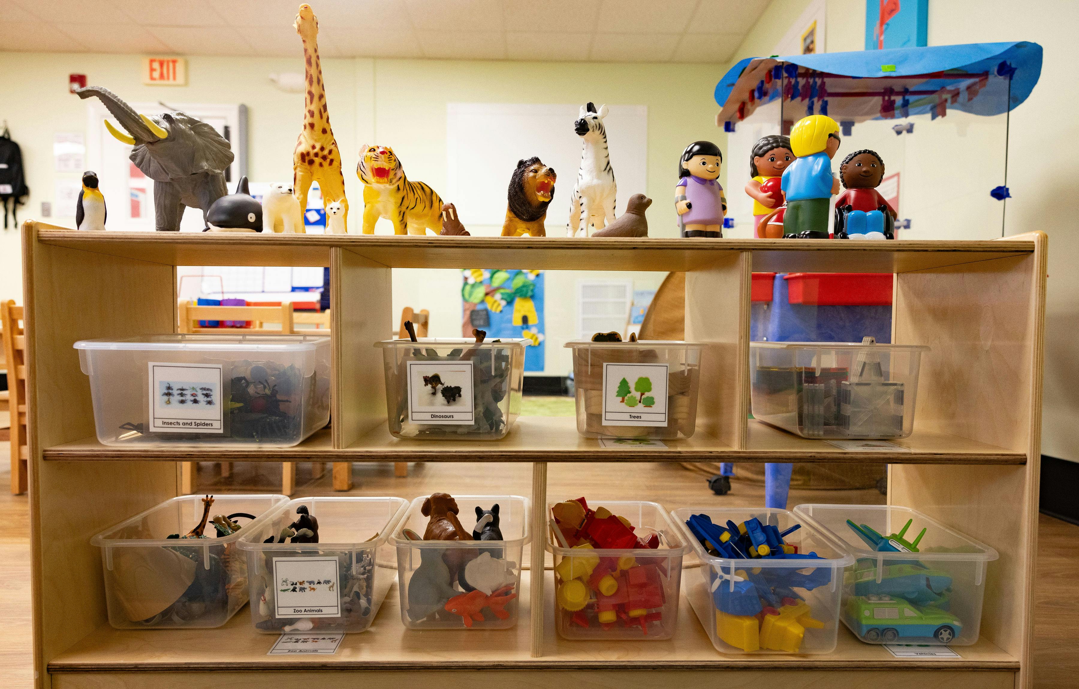 A wooden shelf with various plastic animal toys and bins of toys