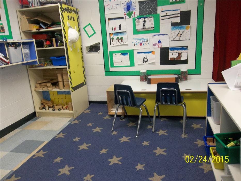 Classroom corner with shelves of toys, small chairs at a desk, and artwork on the wall