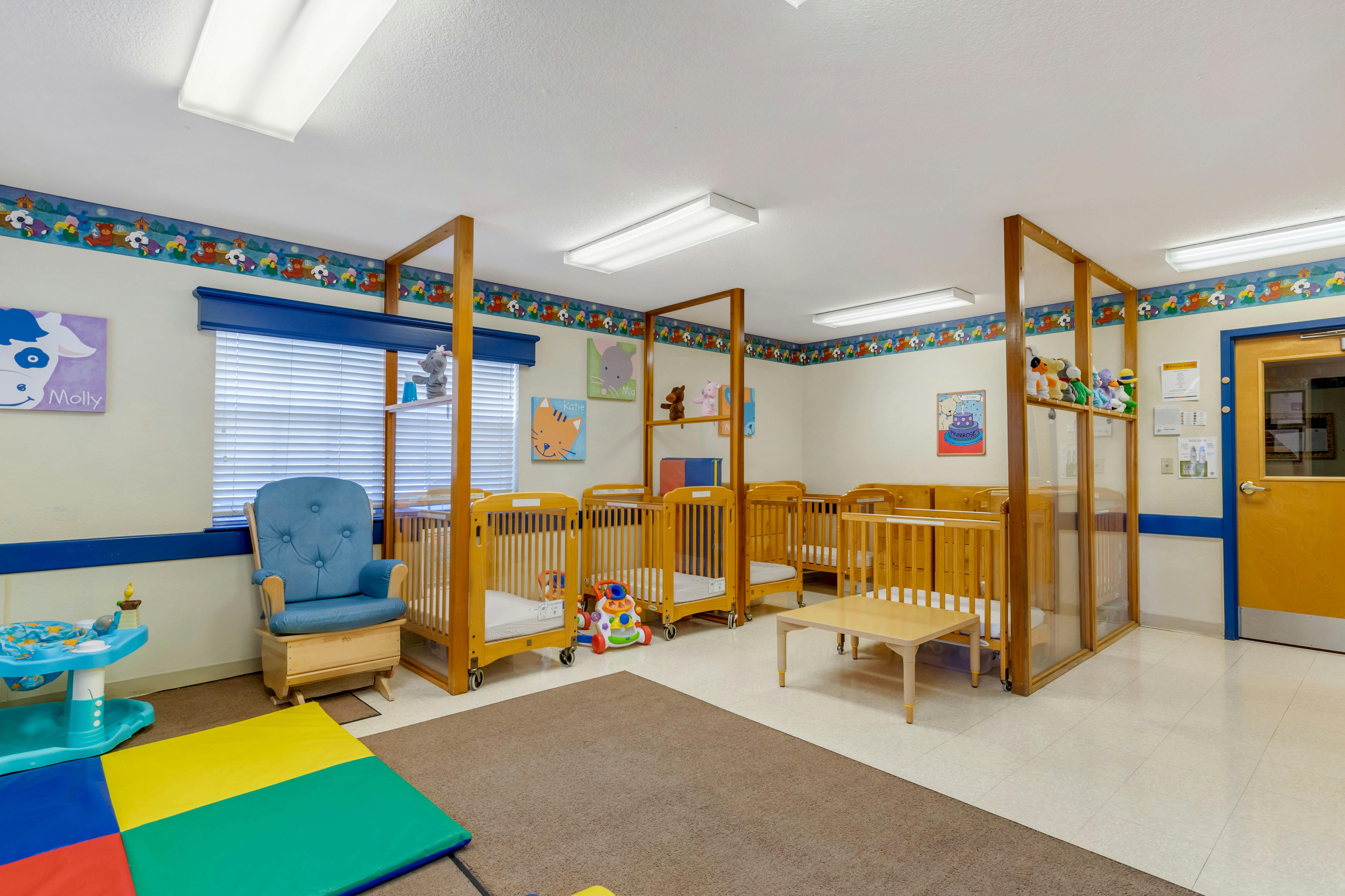 Classroom with multiple wooden cribs, a blue rocking chair, and play mats
