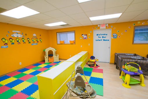 Infant room with colorful floor mats, playhouse, and cribs