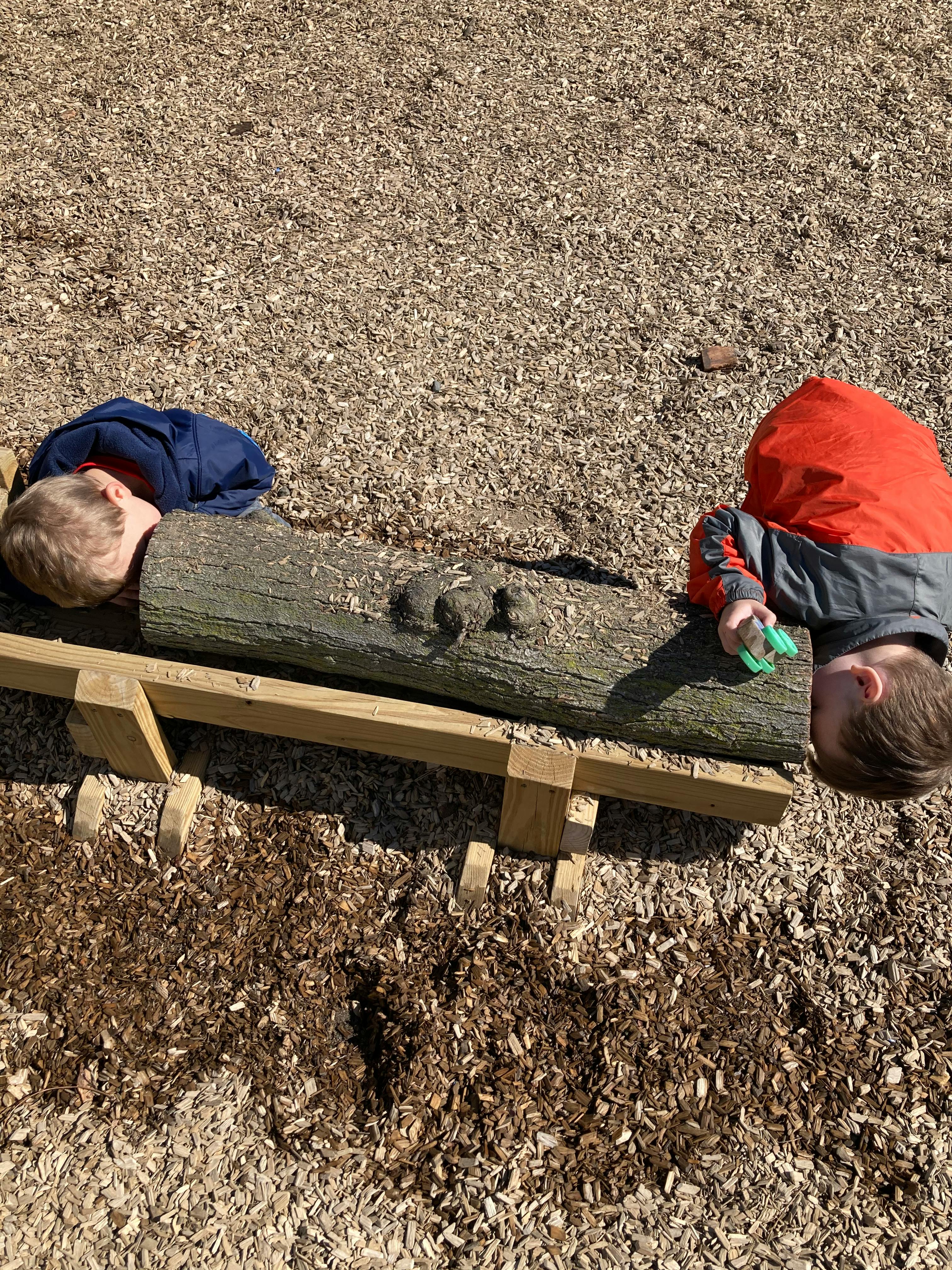 Two children playing with a log on a wooden stand