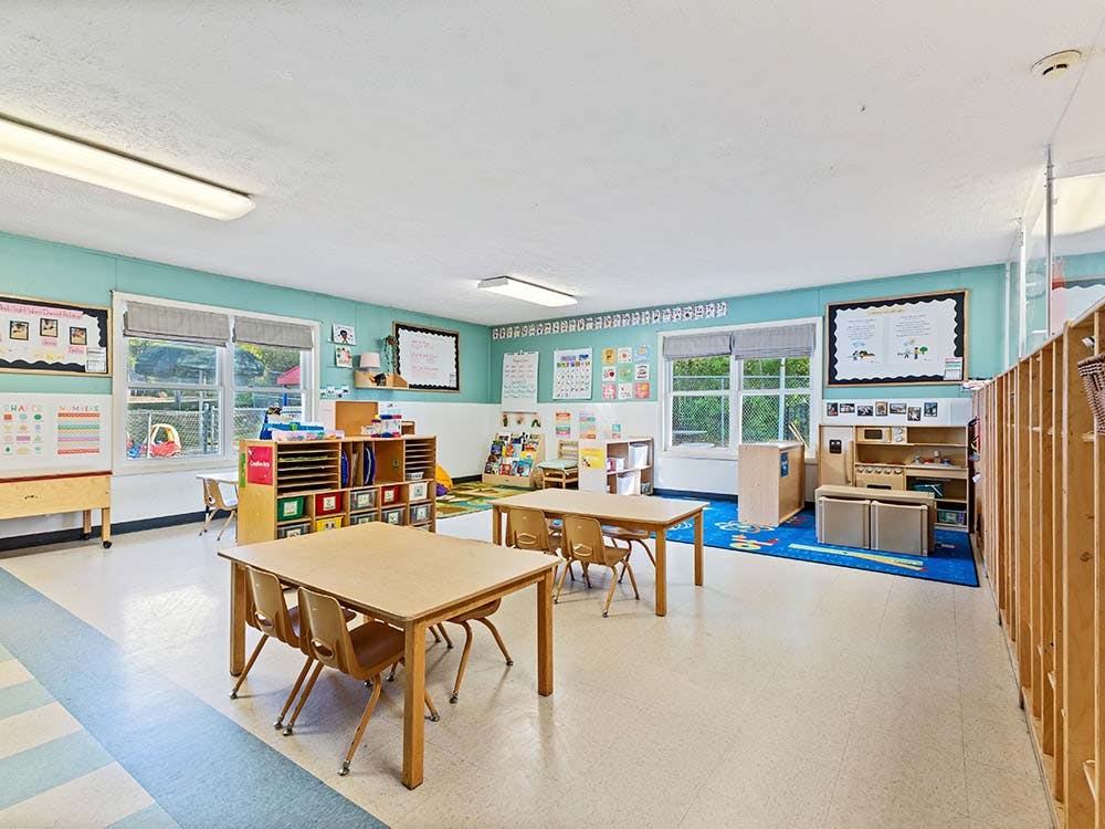 Classroom with small tables and chairs, shelves, and learning posters