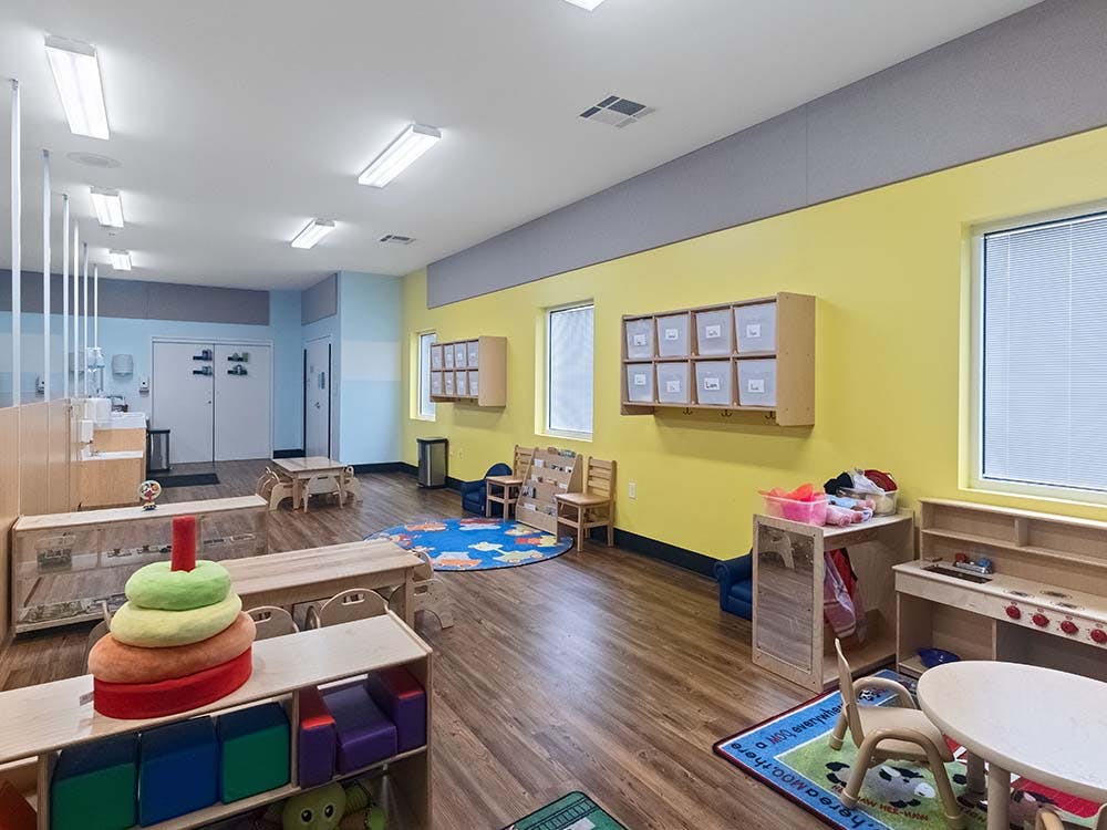 An empty classroom with small tables, chairs, and learning toys