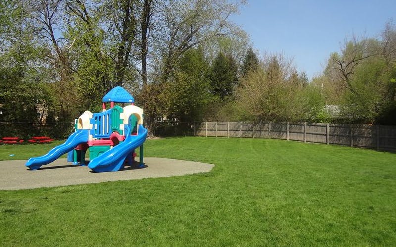 Colorful playground structure with slides on a green lawn with a wooden fence