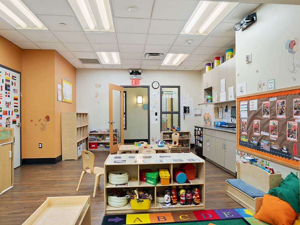 An empty early childhood classroom with cubbies, tables, and a bulletin board