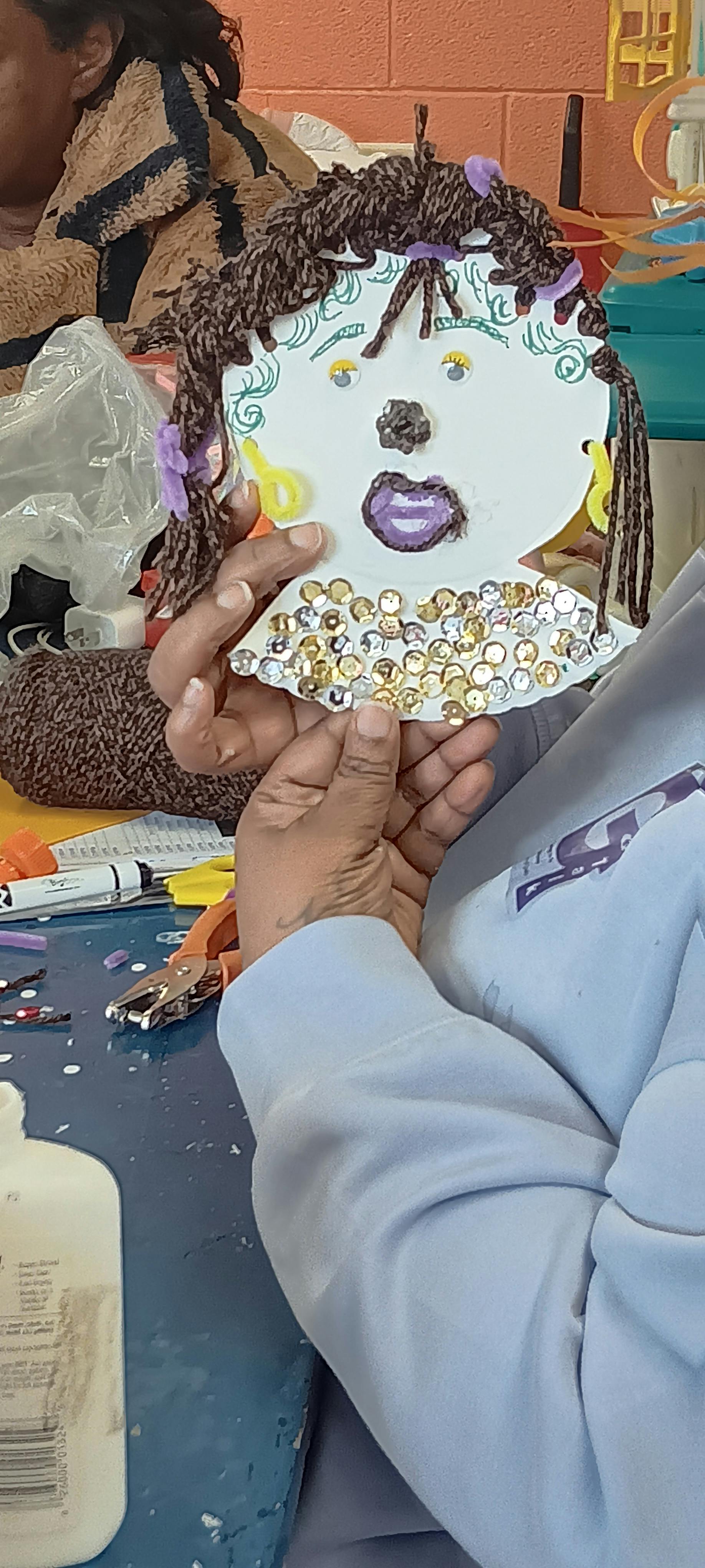Person holding a craft project of a face with yarn hair and sequins