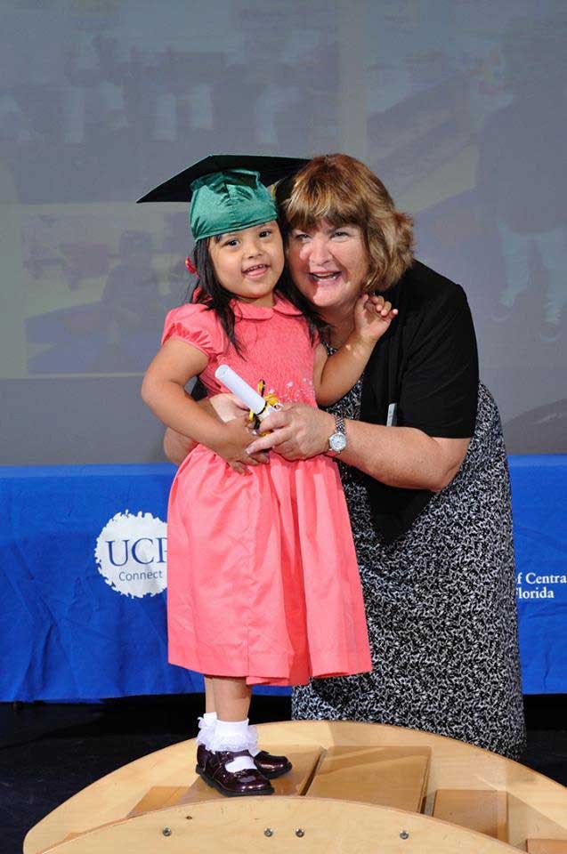 Child in graduation cap and gown holding a diploma with an adult