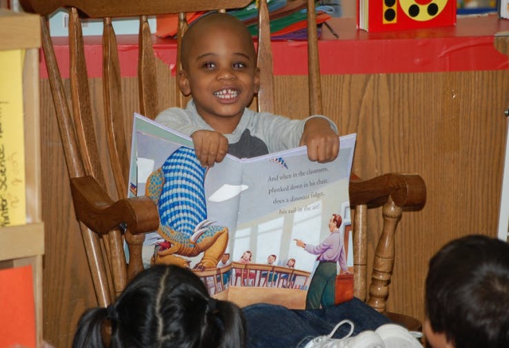 Child sitting in a rocking chair holding an open book