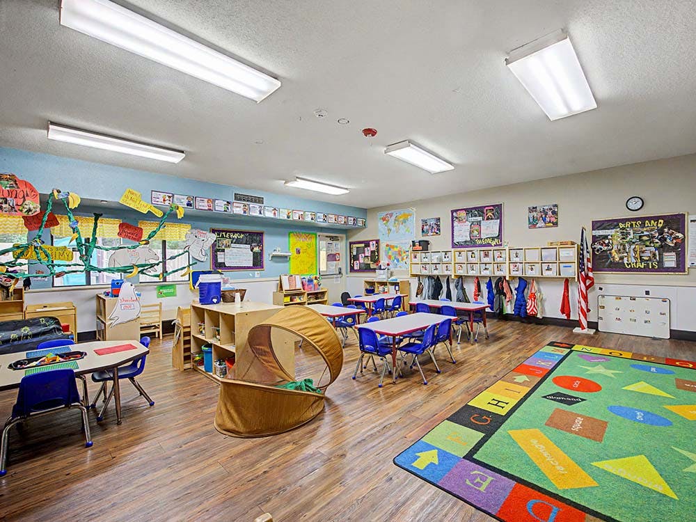 An empty classroom with small tables, chairs, and a colorful rug