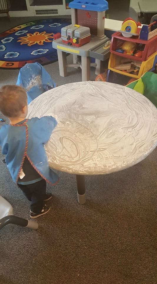 Child in a blue smock painting on a round table