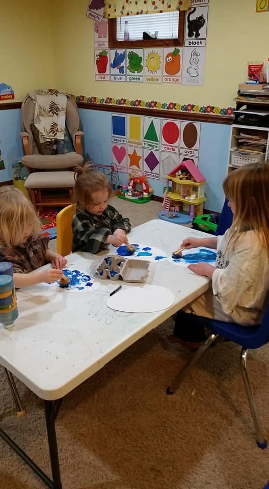 Three children painting at a table in a classroom