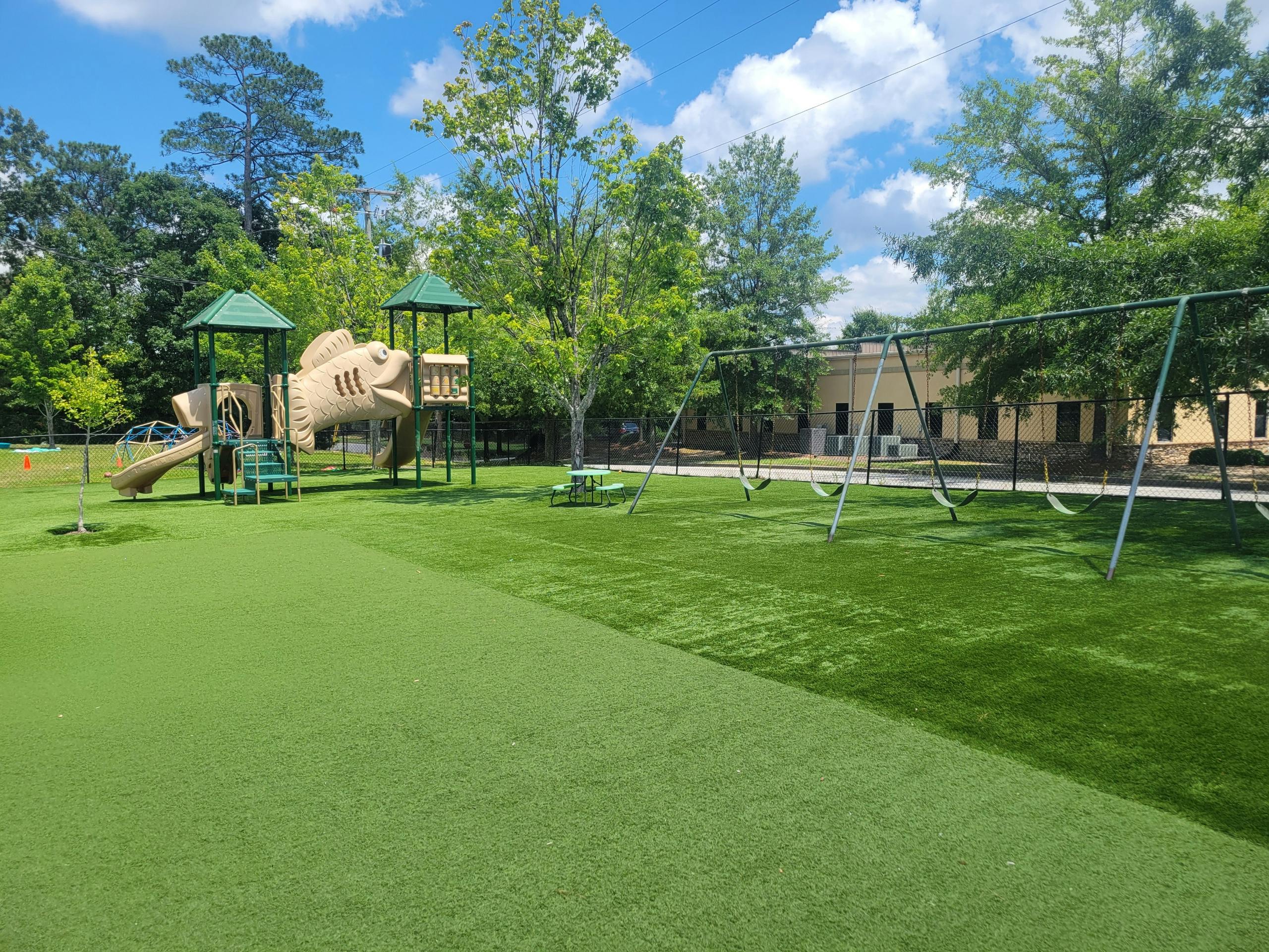 Playground with a fish-shaped play structure and swings on a green turf
