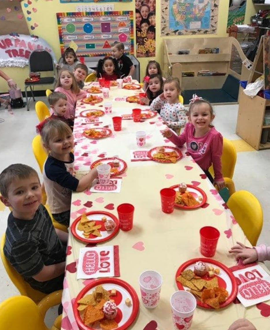 Children sitting at a long table with plates of food and red cups