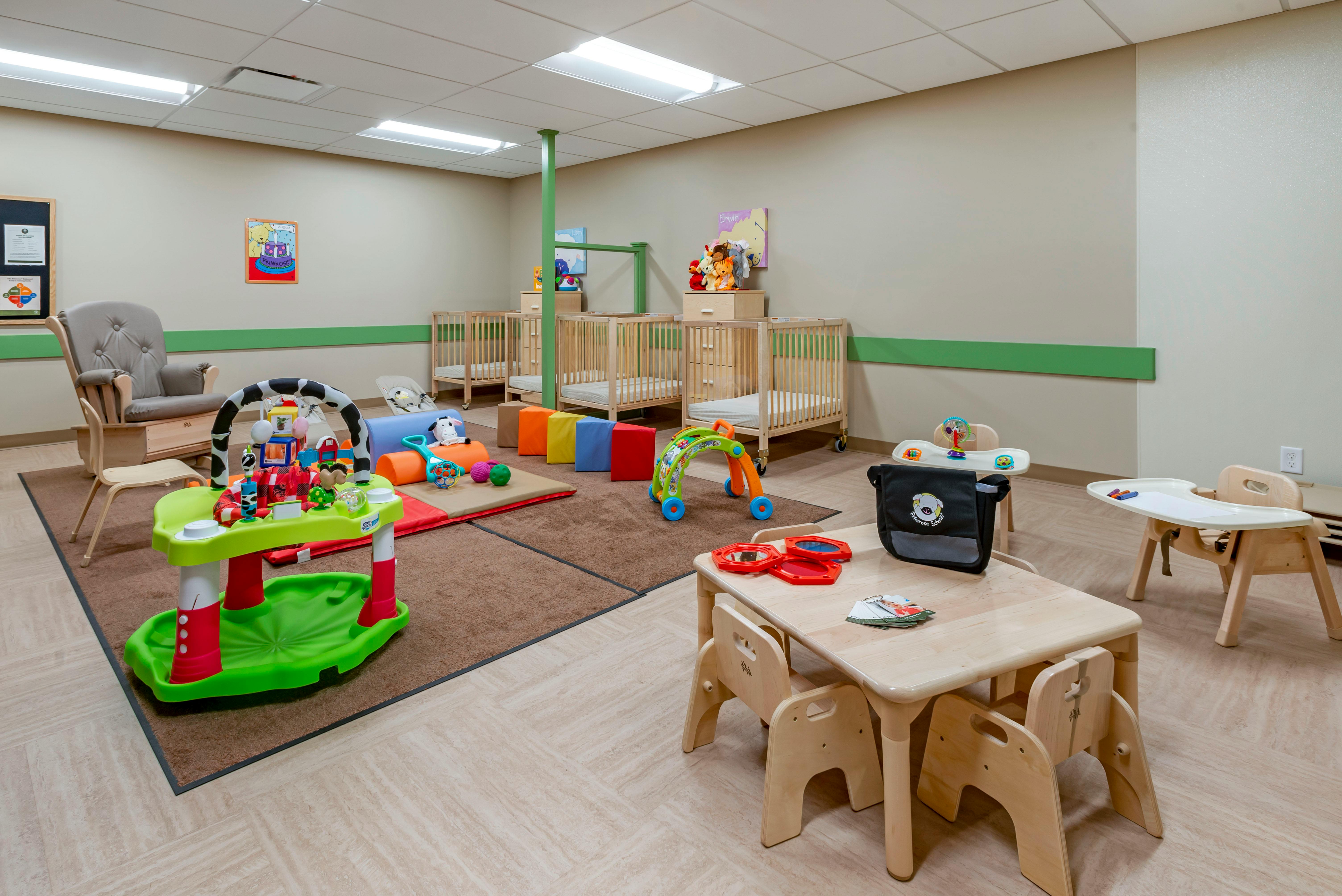 A playroom with cribs, play mats, baby swings, a small table with chairs, and toys