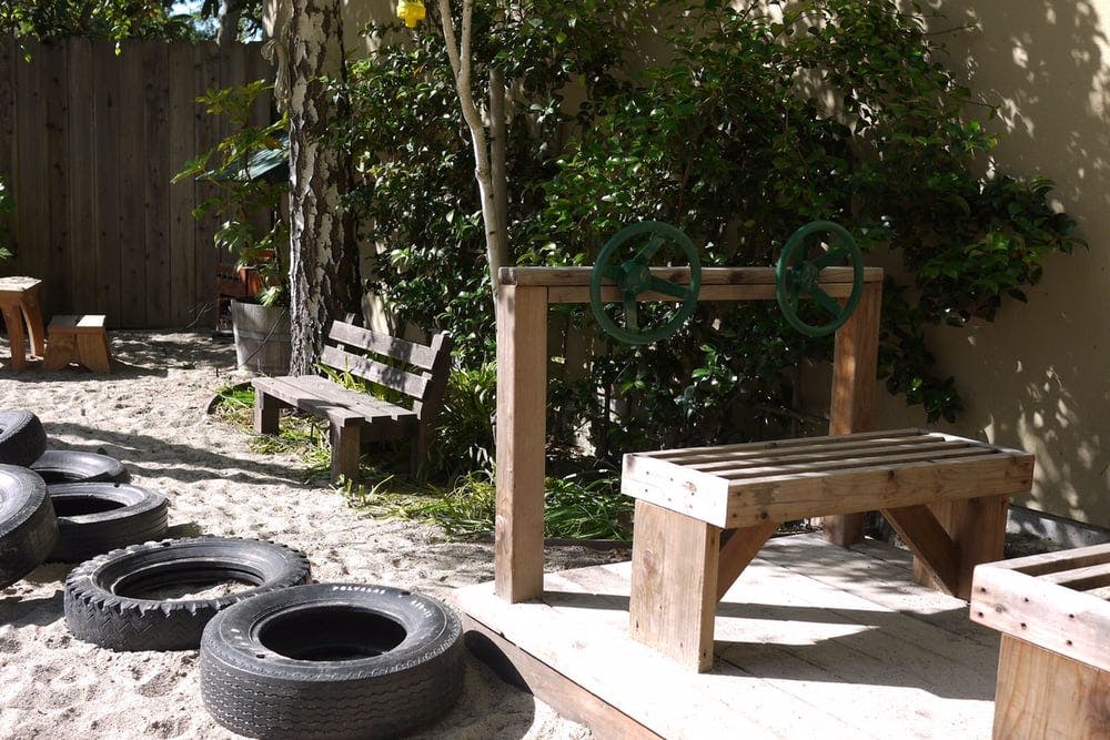 Outdoor play area with tires in sand, wooden bench, and wooden play structure